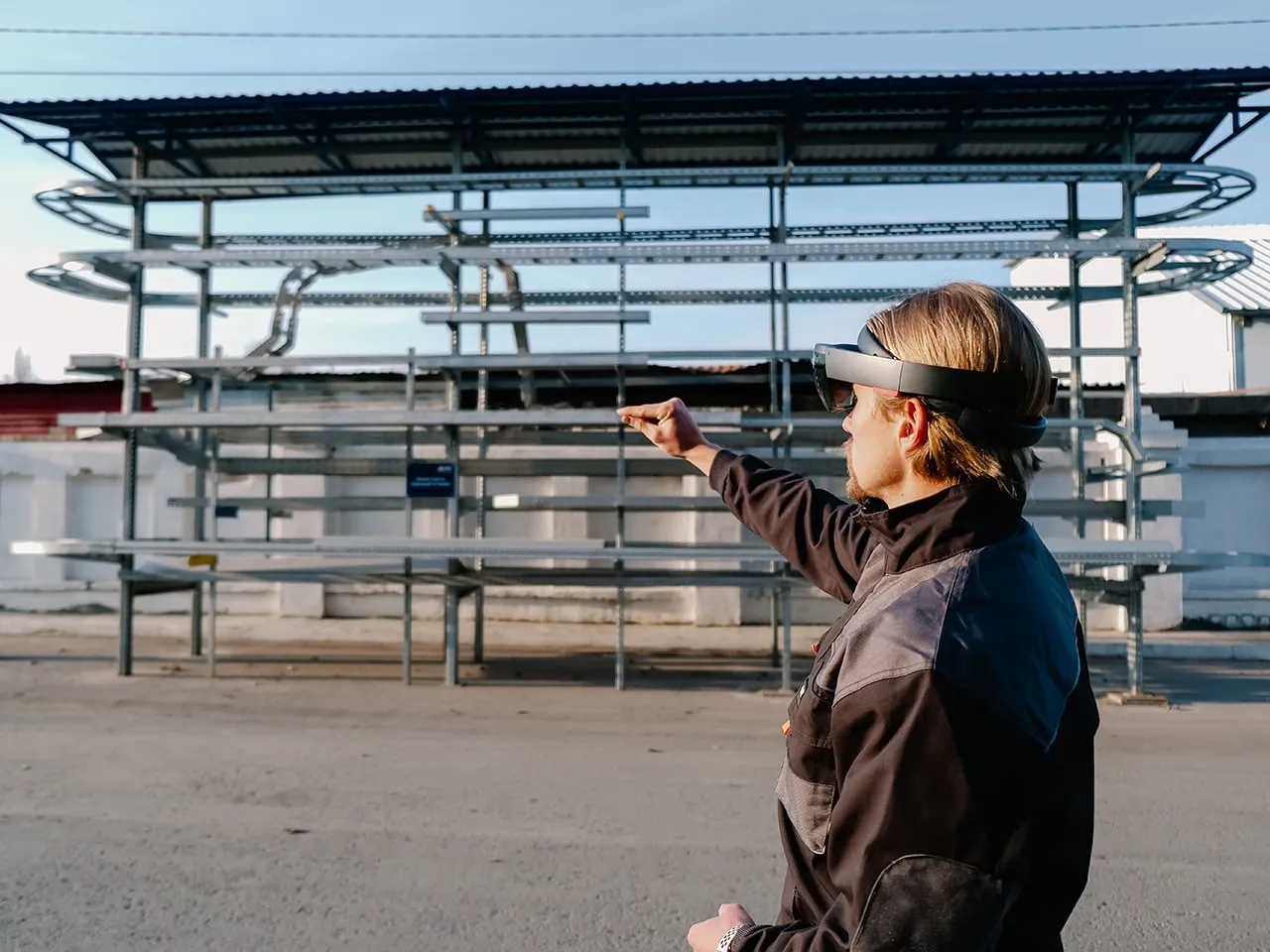 A worker with an AR headset points at a steel rack of cable trays outdoors.