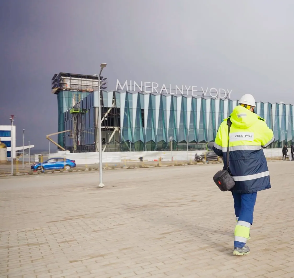 An engineer in a safety vest and helmet walks towards the airport terminal across the apron.