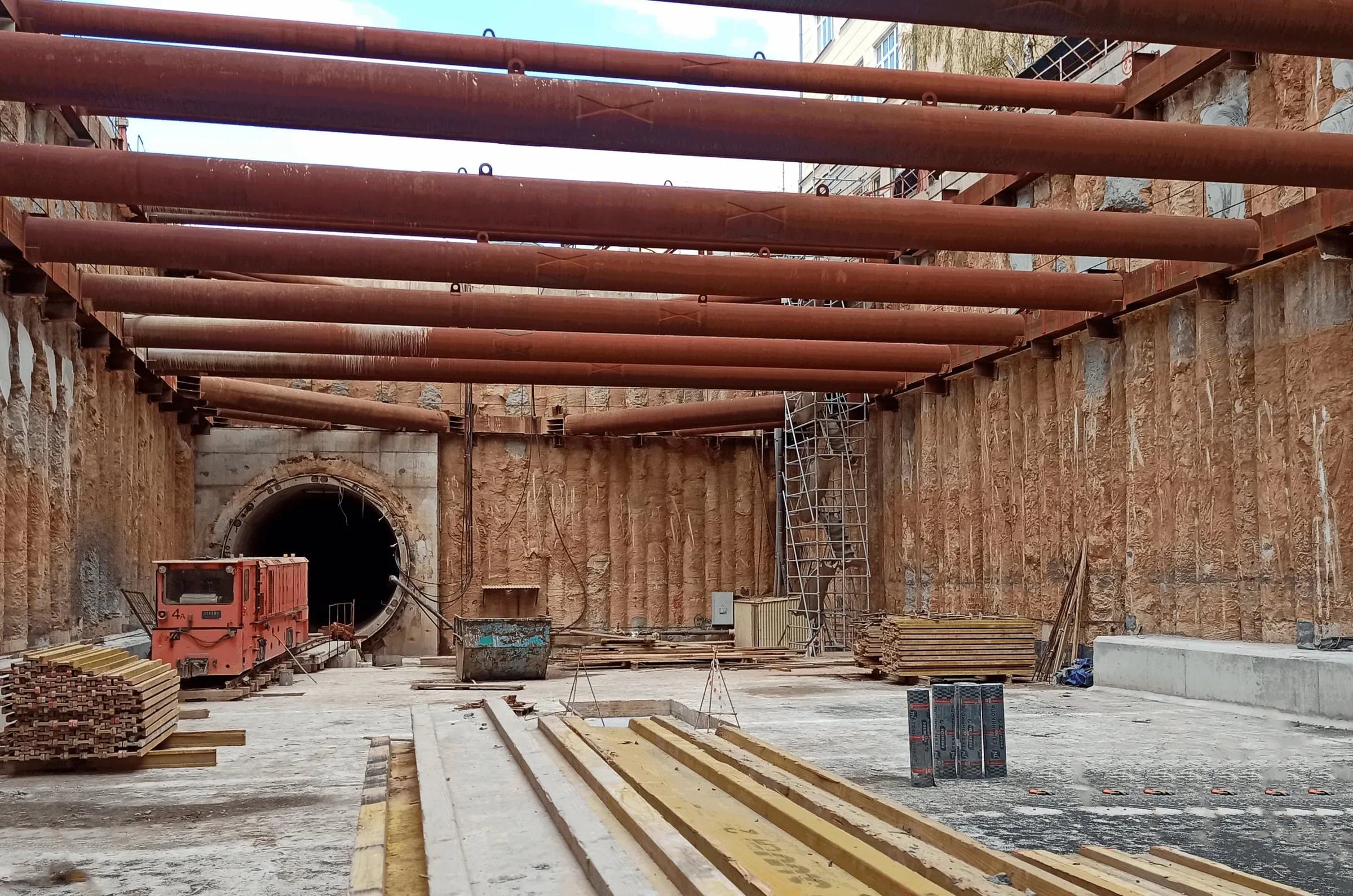 An open excavation for a metro shaft, with large steel struts across the top and a tunnel opening at the far end.