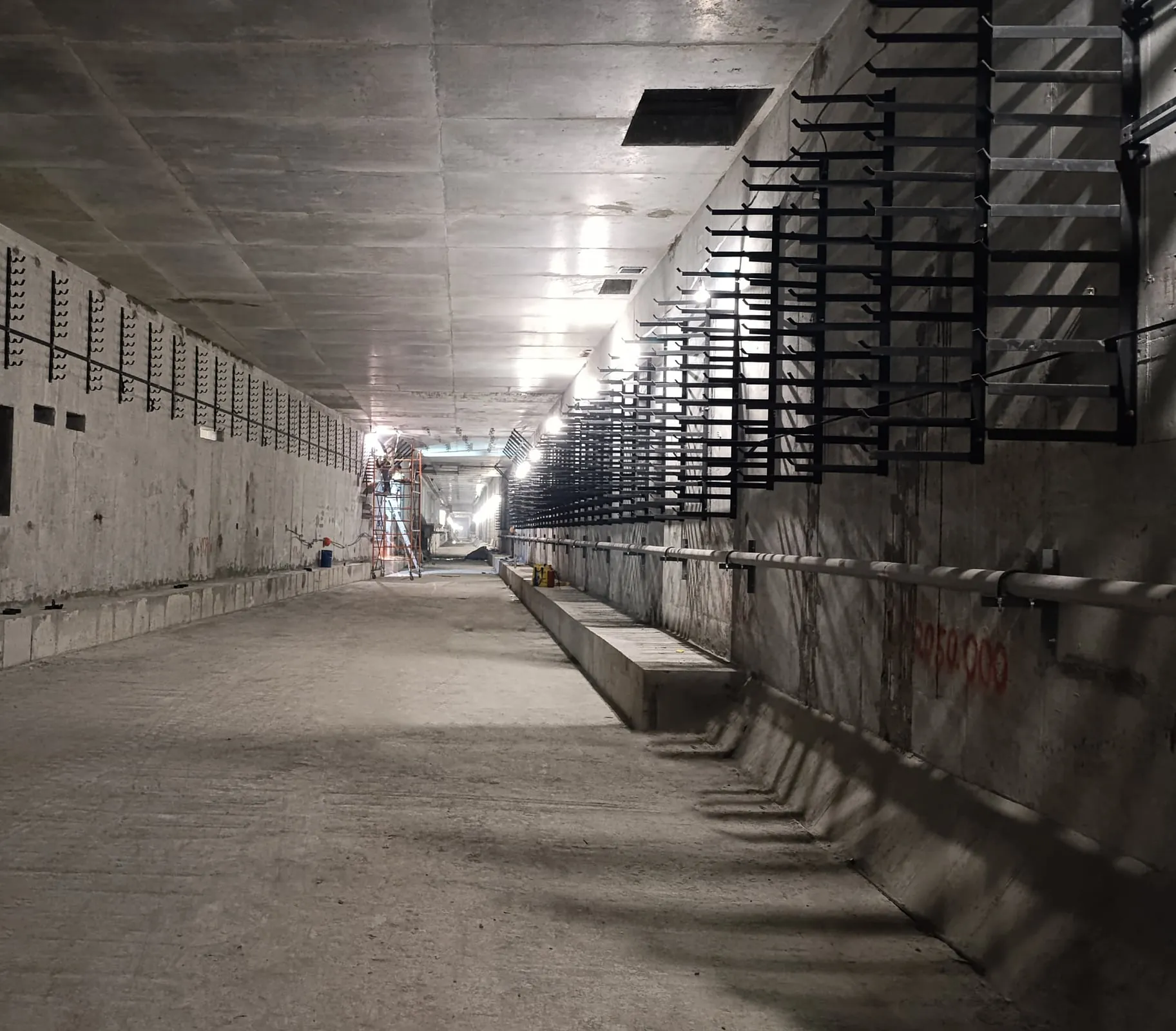 A long concrete metro tunnel under construction, with black cable supports fixed to the wall.